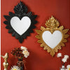 Two ornate heart-shaped wall mirrors, one black and one gold, displayed on a red wall with floral accents.