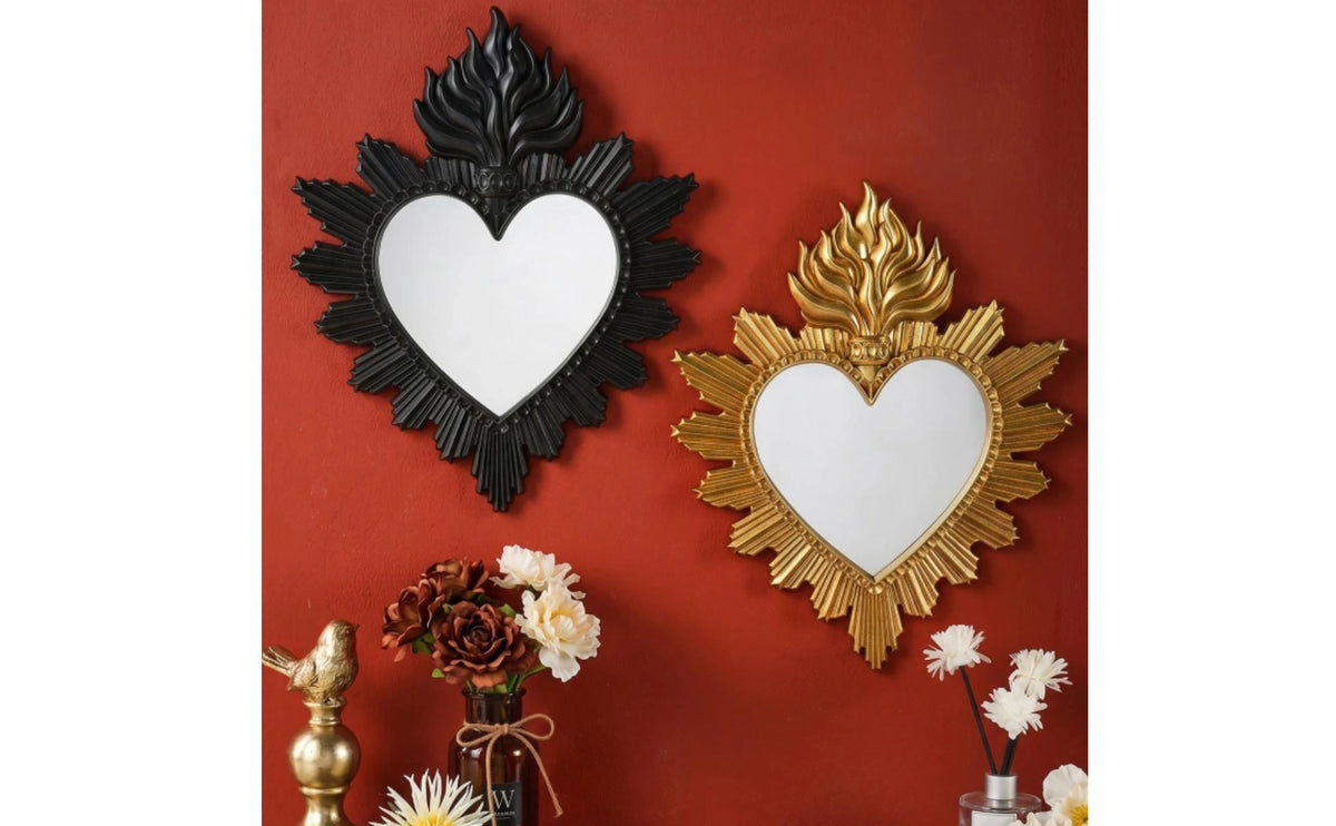 Two ornate heart-shaped wall mirrors, one black and one gold, displayed on a red wall with floral accents.