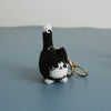 A handcrafted crochet cat keychain pendant with black and white fur against a gray background.