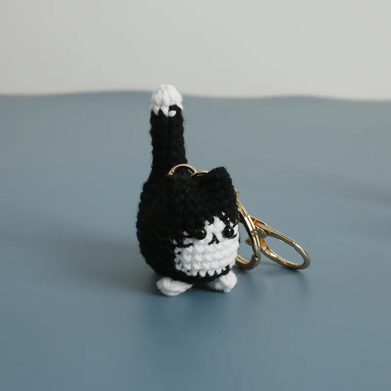 A handcrafted crochet cat keychain pendant with black and white fur against a gray background.