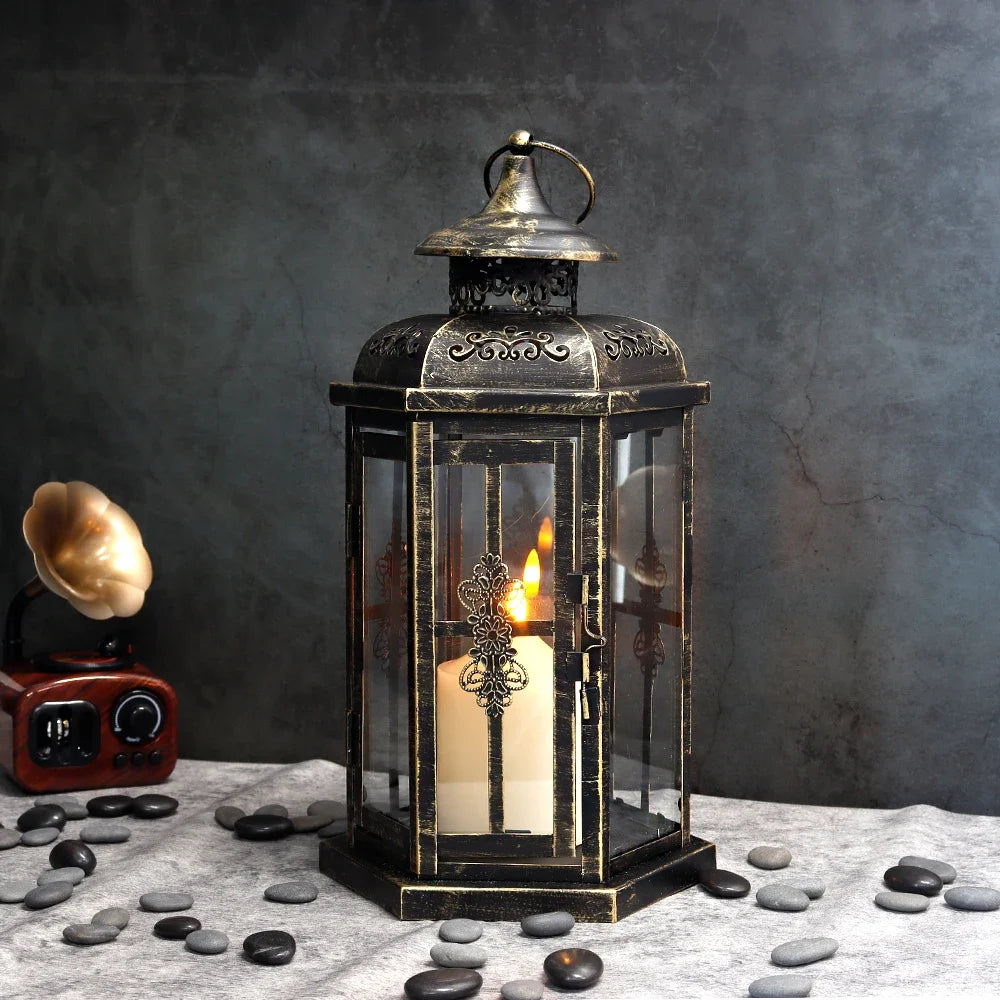 A vintage Nordic iron candle lantern with glass panes sits on a gray cloth surrounded by smooth stones.