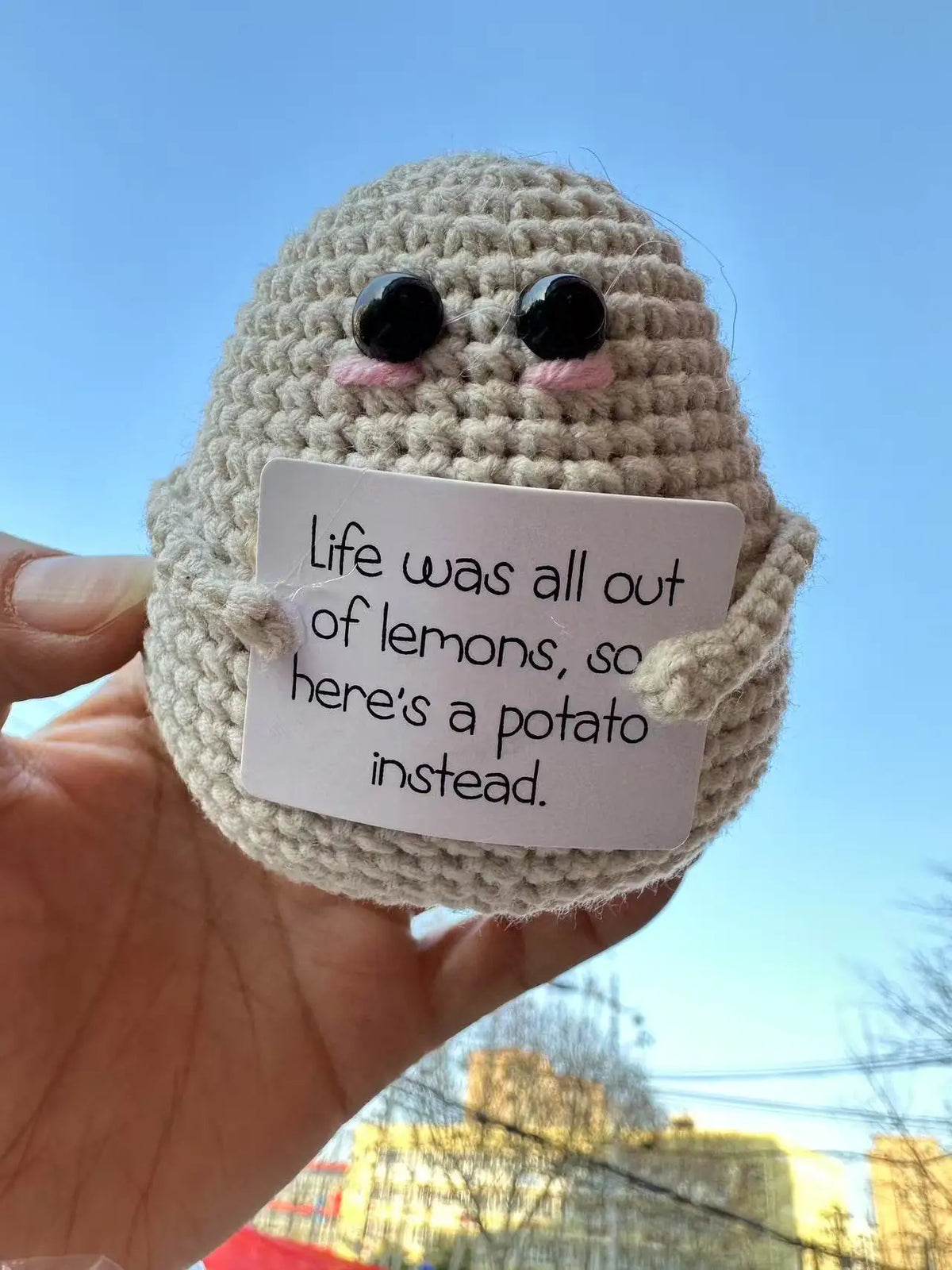 Hand-crocheted brown baseball bat doll with pink facial features holding a card that reads Life was all out of lemons so here