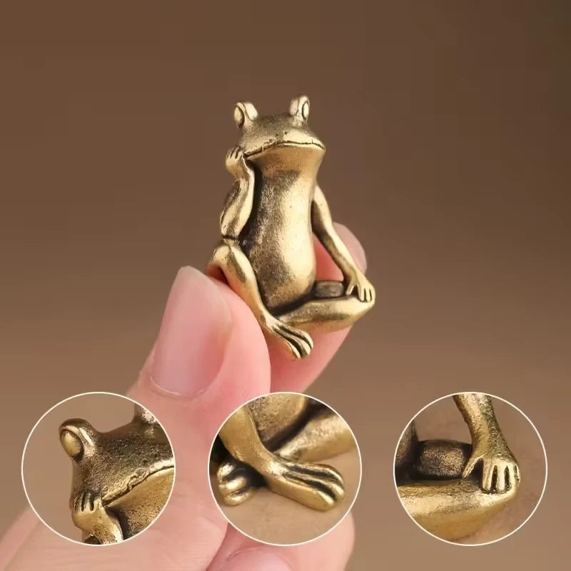 A hand holds a vintage brass frog statue desktop ornament, showing the detail of the animal sculpture.