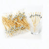A clear plastic bag filled with bamboo fruit skewers featuring silver ball tops, arranged next to a glass.