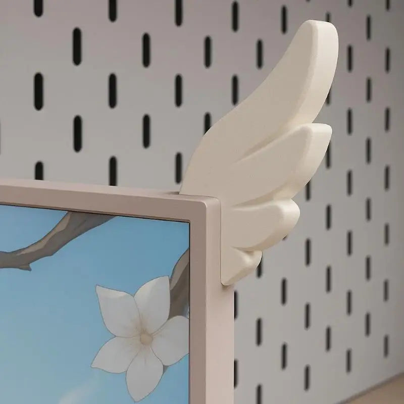 A light beige wing decoration mounted on a monitor frame against a white background with black dots.