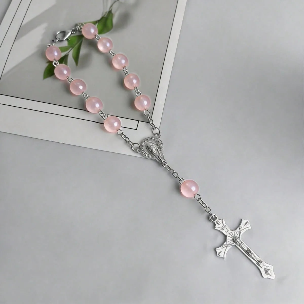 A silver rosary set featuring pink translucent beads and a cross pendant on a white card.