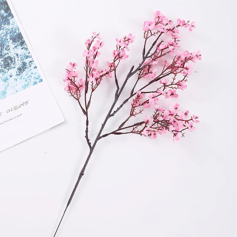 A branch of pink cherry blossoms and white gypsophila artificial flowers on a white background.