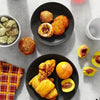 A dark plate holds several golden-brown baked goods, including muffins and pastries, on a light gray surface.