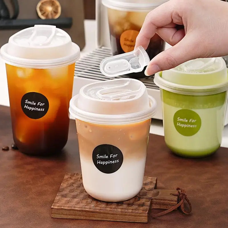 A hand is holding a clear disposable coffee cup with a lid, showing various shades of iced coffee.