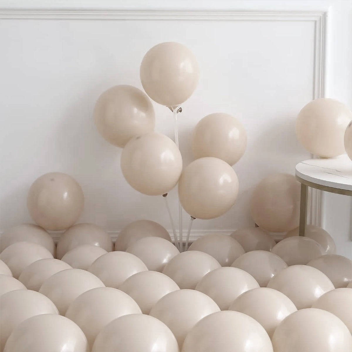 A collection of beige and cream balloons arranged in a balloon arch display against a white wall.