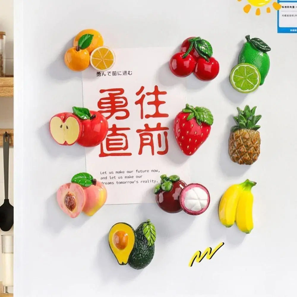 A display of colorful fruit magnets featuring apples, strawberries, pineapples, and citrus fruits on a white background.
