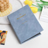 A light blue photo album titled The Moment resting on a white surface next to yellow flowers and a calendar.