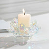 A clear crystal lotus flower candle holder with a white pillar candle and flame on a white surface.