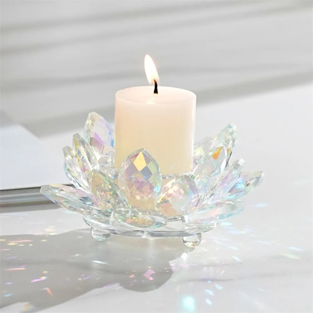 A clear crystal lotus flower candle holder with a white pillar candle and flame on a white surface.