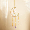 A golden crescent moon crystal suncatcher with dangling prism beads hanging against a light background.