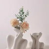 A white ceramic figural vase with an artistic human form holds dried flowers and greenery.