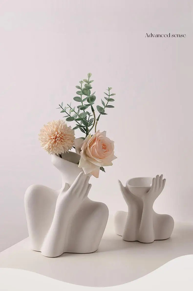 A white ceramic figural vase with an artistic human form holds dried flowers and greenery.