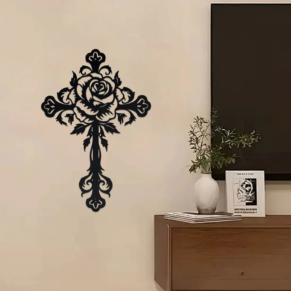 Black decorative metal rose cross wall art mounted on a light wall above a wooden cabinet.