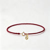 A handmade red string bracelet with a gold-plated clasp, laid flat on a white background.