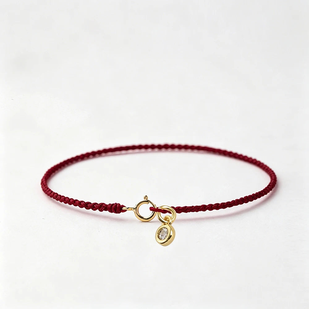 A handmade red string bracelet with a gold-plated clasp, laid flat on a white background.
