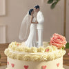 Elegant bride and groom wedding cake topper featuring a white cake with pink roses and heart decorations