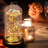 Une rose de verre éternelle avec un tige doré et des lumières LED est exposée sur une surface sombre à côté d'une bougie.