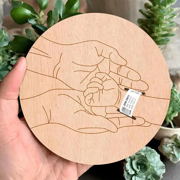 A hand holds a wooden outline of a baby's handprint, designed as a personalized newborn hospital keepsake sign.