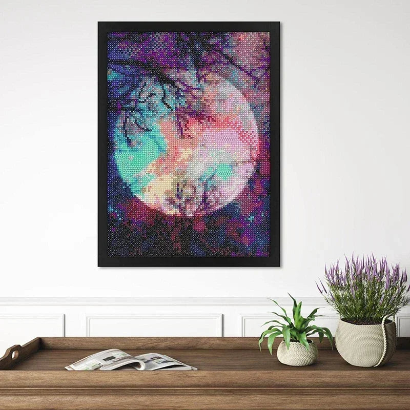 A framed piece of diamond art featuring a vibrant pink and purple moon against a dark background.