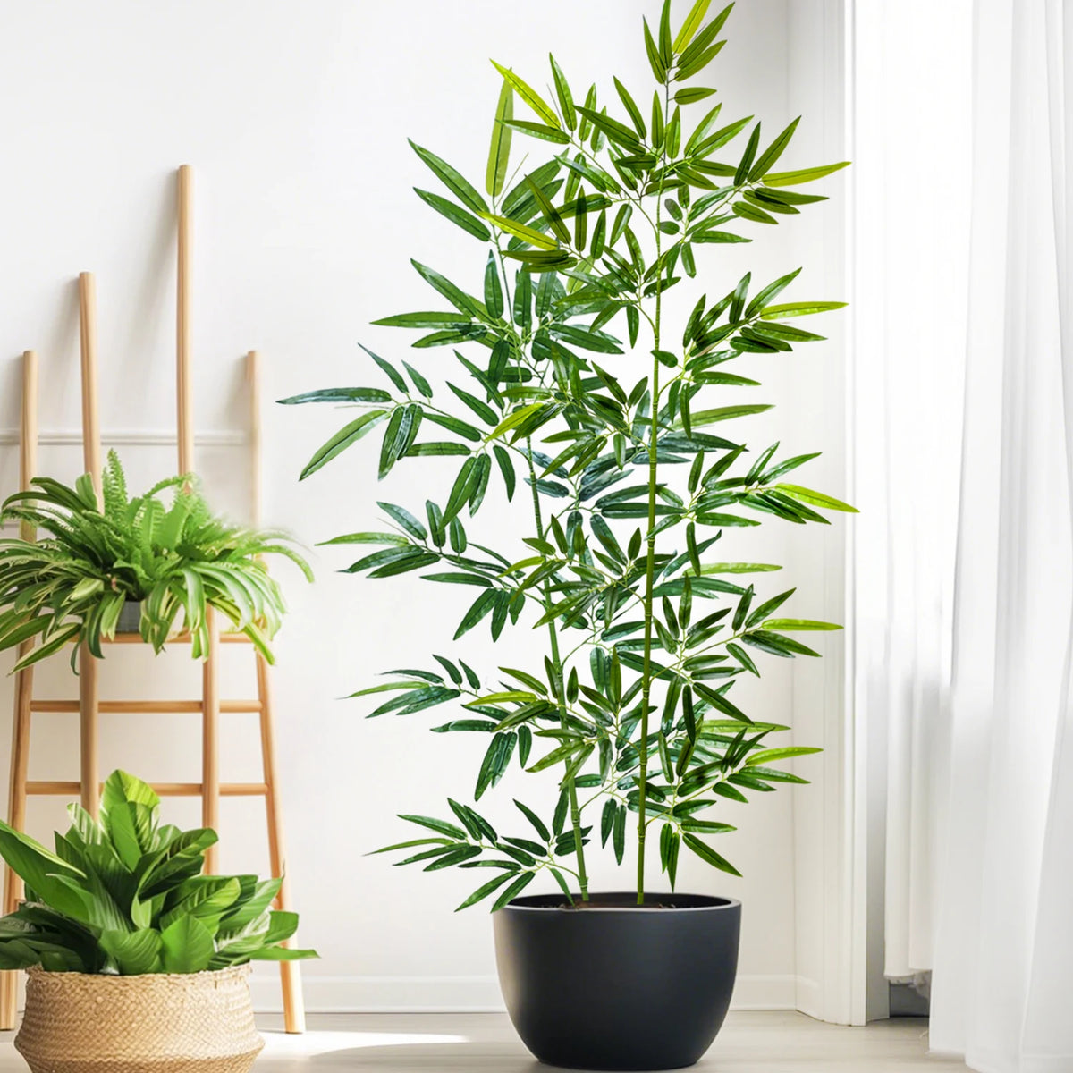 A tall artificial bamboo branch with green leaves displayed in a black pot against a white background.