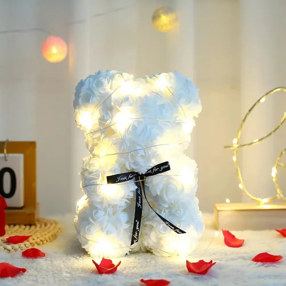 A white artificial rose teddy bear illuminated with warm lights resting on a white surface.