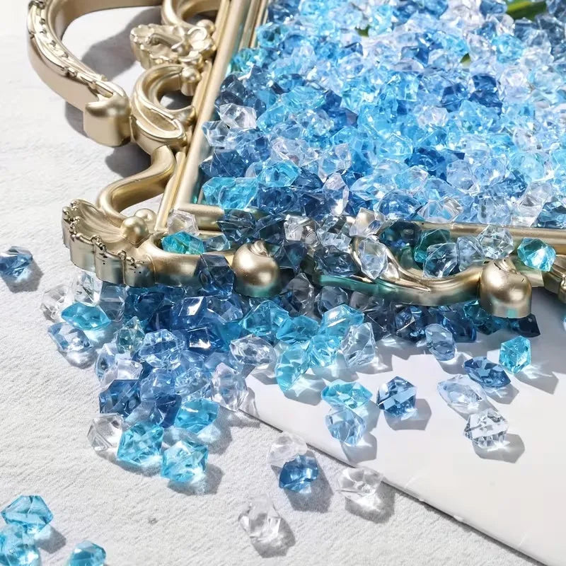 A close-up of crushed blue acrylic pebbles displayed in a gold-toned decorative frame on a white surface.