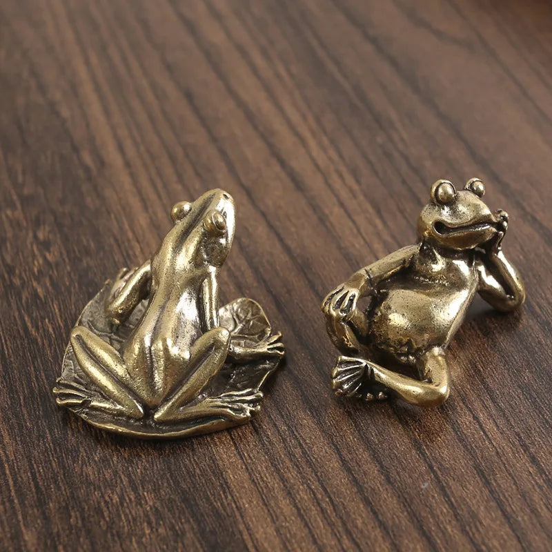 Antique brass frog sculpture decor resting on a dark wooden surface.