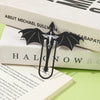 A black metal bookmark shaped like a four-winged dragon resting on white books.