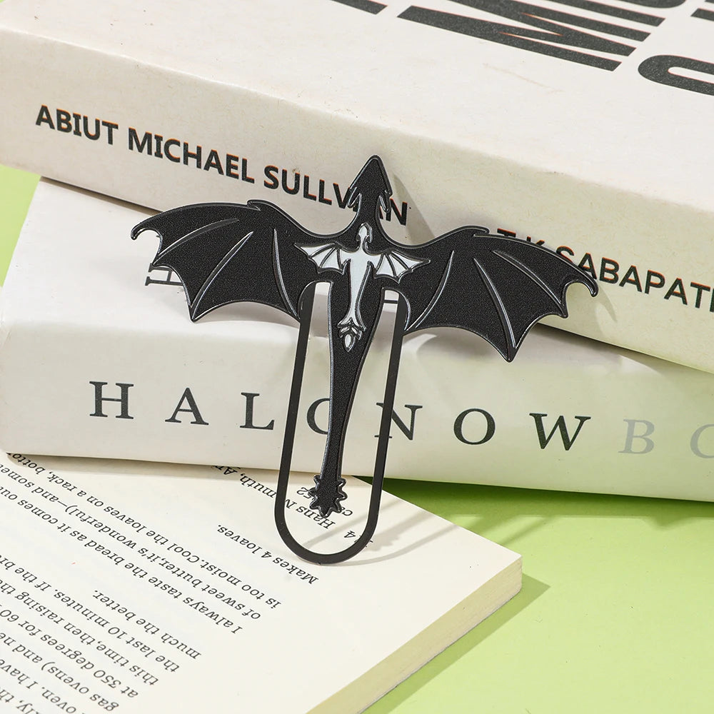 A black metal bookmark shaped like a four-winged dragon resting on white books.