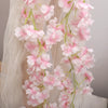 A delicate garland of pink artificial sakura flowers draped against a sheer white background.
