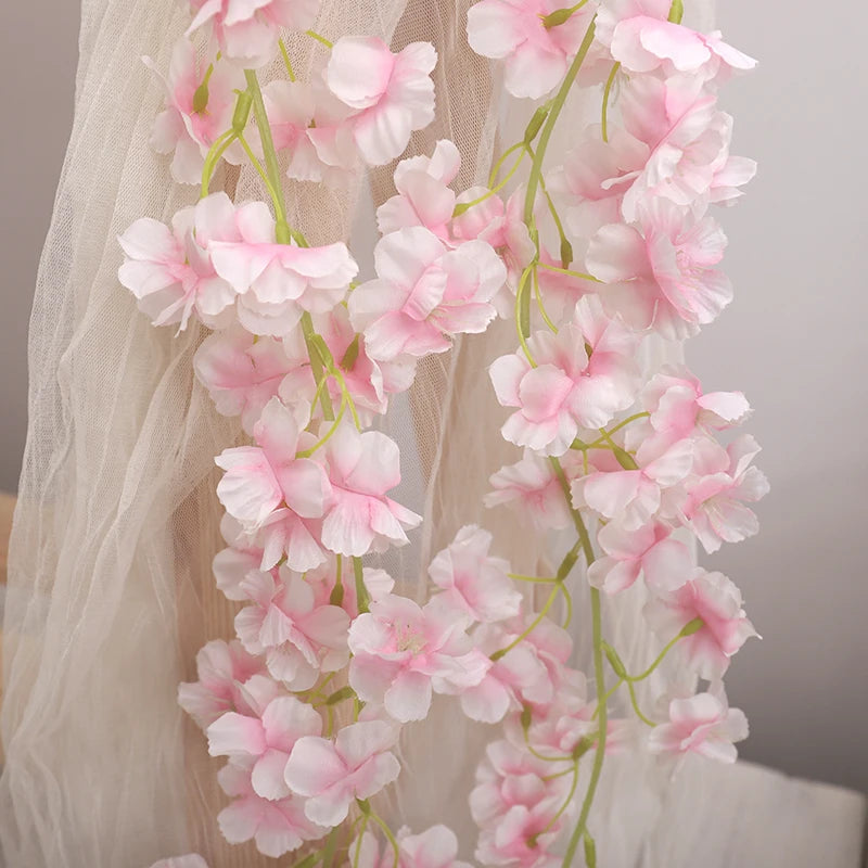 A delicate garland of pink artificial sakura flowers draped against a sheer white background.