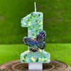 A number candle shaped like '1' covered in green sequins and featuring a butterfly decoration.