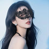 A woman with long dark hair wearing a black lace floral eye mask and silver earrings against a light blue background.
