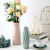 A pink vase holds floral arrangements next to a light green decorative vase and a white cup.