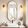 A bathroom vanity featuring an oval mirror with a gold frame, a white vessel sink, and natural light fixtures.