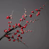 A branch of artificial plum blossoms with red flowers against a gray background.