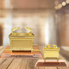 A golden metal statue of the Ark of the Covenant resting on a wooden surface.