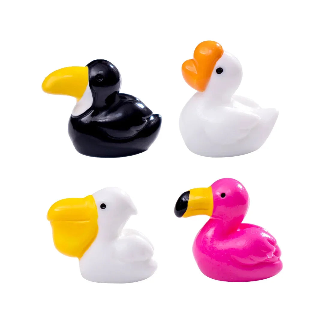 Trois petites sculptures d'animaux en résine : un canard noir, un canard blanc et un canard rose avec des accents jaunes.