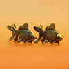 A pair of retro brass goldfish statues resting on a smooth orange surface.