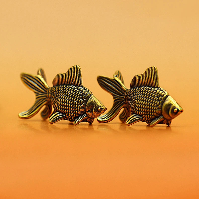 A pair of retro brass goldfish statues resting on a smooth orange surface.