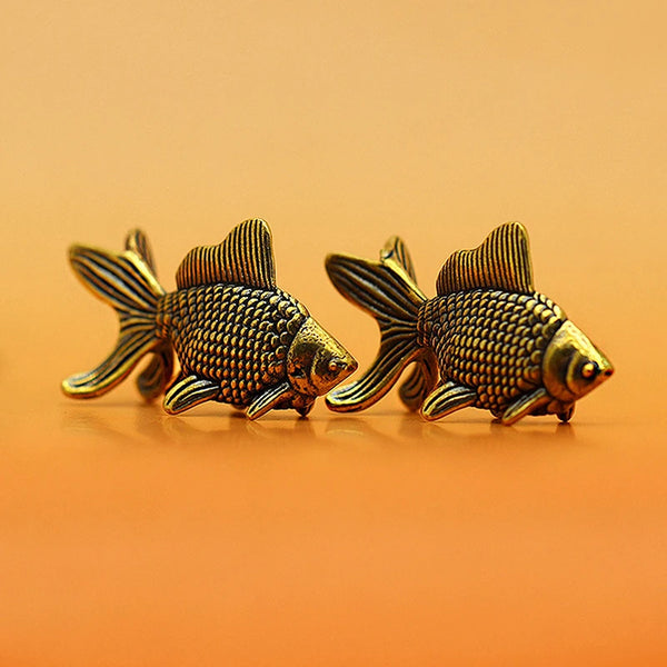 A pair of retro brass goldfish statues resting on a smooth orange surface.