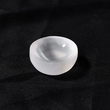 A smooth, translucent white selenite bowl resting on a dark surface.