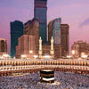 A panoramic view of a large mosque complex with modern skyscrapers in the background, featuring a large crowd in the foregrou