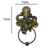 A bronze-colored octopus skull door knocker with a cast iron ring.