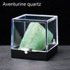 A clear display box holds a green aventurine quartz crystal specimen on a dark surface.